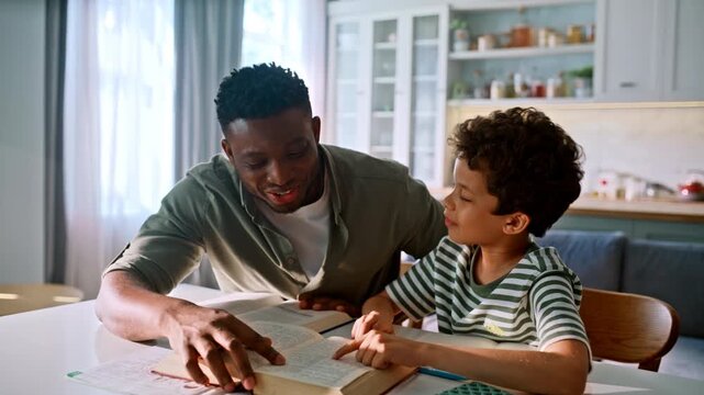 Black father son reading encyclopedia kitchen. Boy studying with smiling dad.