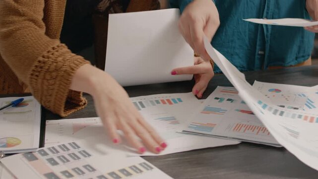 Charts, analysis and teamwork in a close-up of two colleagues pointing to pie diagrams and bar graphs on scattered printouts. Hands-on report comparison for business decisions, research and planning.