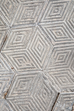 Weathered geometric concrete paving tiles form a repeating three-dimensional sidewalk pattern