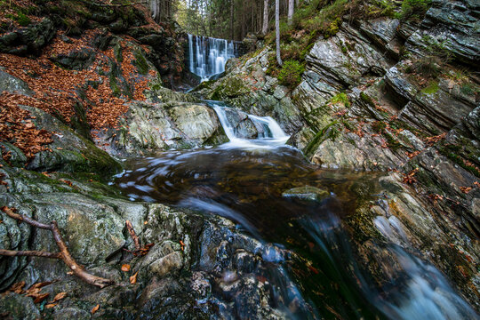 Small cascading waterfall flowing over rugged rocks in an autumnal forest landscape