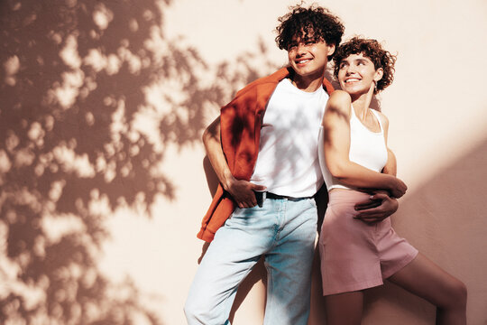 Young smiling beautiful woman and her handsome boyfriend in casual summer clothes. Happy cheerful family. Female having fun. Couple posing in street at sunny day. Near wall at sunset