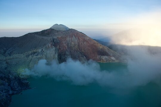 Ijen volcano crater at sunrise with turquoise acidic lake, drifting sulfur steam and warm morning light, East Java, Indonesia