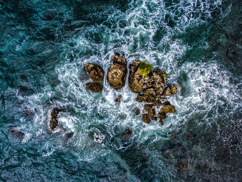 Aerial top down view of ocean waves crashing on sea rocks