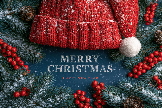 red knit santa hat with merry christmas text on snowy fir branches