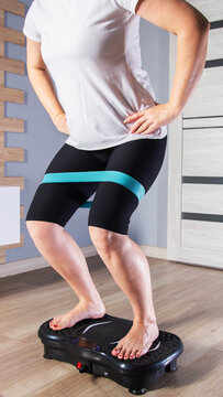 Person doing squats on a vibration plate with a resistance band around thighs, engaging in home fitness workout for muscle strengthening and body toning indoors vertical photo