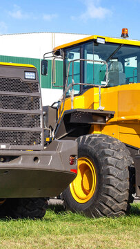 Yellow heavy construction machine with large tires and cabin on grass field, industrial equipment display under blue sky, outdoor display vertical photo