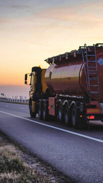 Heavy duty tanker truck moving at high speed on open road during twilight hour. Large vehicle transporting liquid cargo with glowing sky backdrop. Transportation concept vertical photo