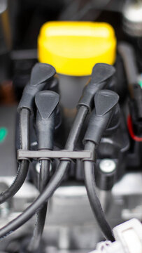Close-up detail of automotive engine spark plug wires and electrical connections, showing black rubber boots and a blurred yellow fluid cap in background, mechanical system vertical photo