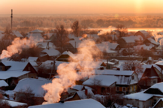 Winter village landscape at sunrise, sun illuminating frosty forest and frozen river, smoke plumes rising from chimneys of snow-covered houses, tranquil morning scene.
