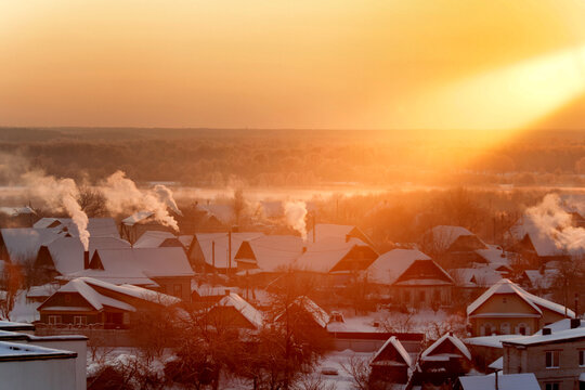Winter village landscape during golden sunrise, snow-covered rooftops, smoke rising from chimneys, cold morning atmosphere