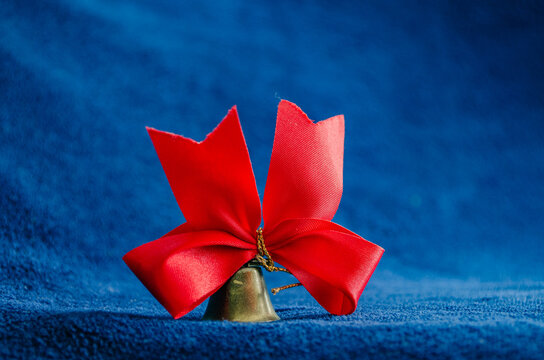 Red ribbon bow tied around a small brass bell on blue fabric