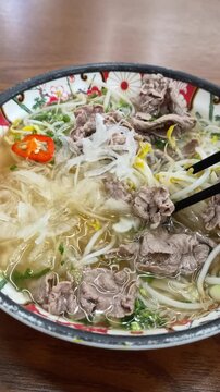 젓가락으로 쌀국수 면발과 소고기, 숙주를 집어 올리는 모습 (Chopsticks holding rice noodles with beef and bean sprouts in pho bowl)