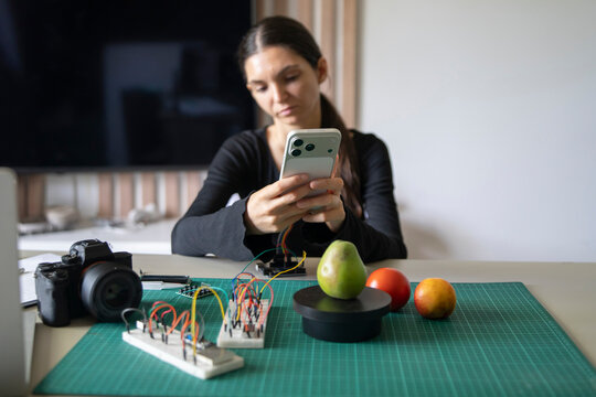 Woman coding AI scale module on smartphone, preparing educational content for online robotics class.
