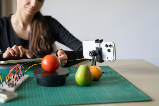 Close up of a smartphone AI camera recognizing tomato and pear while woman codes machine learning app on tablet.
