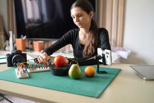 Female developer testing smartphone AI camera recognition artificial intelligence module with tomato and pear.