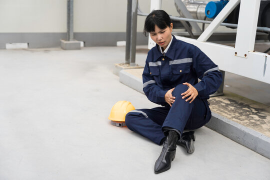 Asian woman worker sitting outdoor holding injured knee in severe pain after workplace accident on construction site