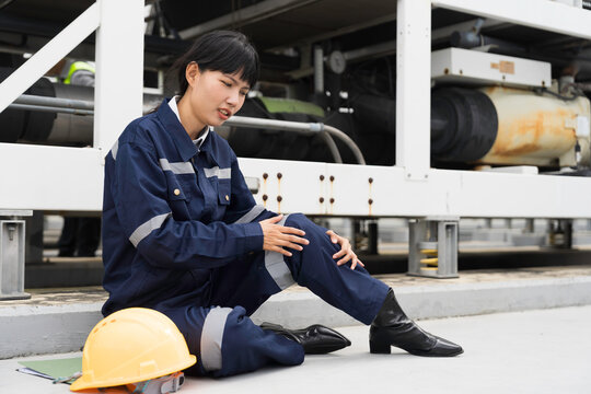 Asian woman worker sitting outdoor holding injured knee in severe pain after workplace accident on construction site