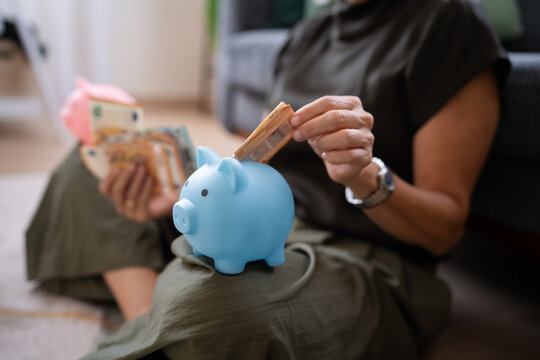White person saving money by inserting euro banknote into blue piggy
