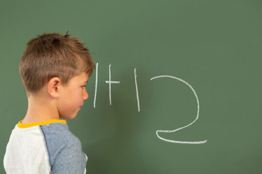 Schoolboy doing math on green chalkboard in a classroom