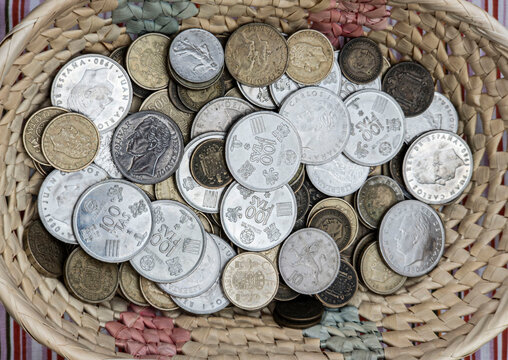 Pedreguer, Spain - August 19, 2026.Top view of a woven wicker basket filled with various vintage Spanish coins, including old pesetas and collectible money
