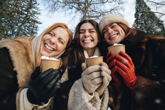 Women and friends hold takeaway cups in winter sunshine