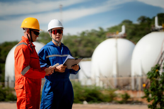 two professional engineer, worker, technician use clipboard discuss work, discussing operations at a gas storage facility. protective uniforms and helmets. industry, engineer, safety, teamwork, energy