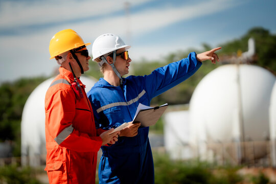 two professional engineer, worker, technician use clipboard discuss work, discussing operations at a gas storage facility. protective uniforms and helmets. industry, engineer, safety, teamwork, energy