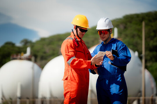 Industrial engineering and workplace safety concept. Two energy plant workers communicating during inspection at a gas storage facility outdoors. engineer, industry, safety, teamwork, energy
