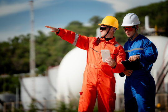 two professional engineer, worker, technician use clipboard discuss work, factory plant industry at a gas storage facility. protective uniforms and helmets. industry, engineer, safety, teamwork.