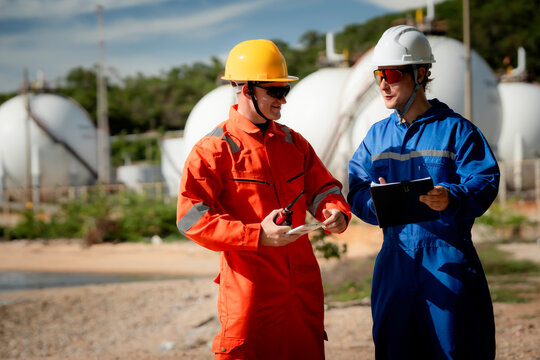 two professional engineer, worker, technician use clipboard discuss work, factory plant industry at a gas storage facility. protective uniforms and helmets. industry, engineer, safety, teamwork.