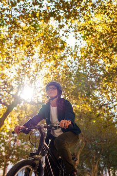 Hispanic woman riding bicycle in sunlit M&aacute;laga park with autumn leaves
