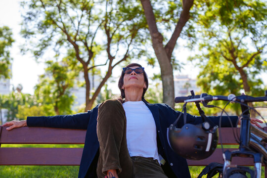Hispanic woman relaxing on bench with bicycle in M&aacute;laga park
