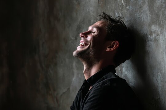 Portrait of a blissful man in his 40s laughing while standing against bare concrete or plaster wall