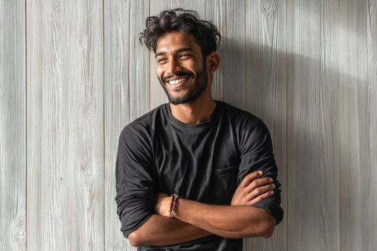 Portrait of a grinning indian man in his 20s with arms crossed isolated on light wood minimalistic setup