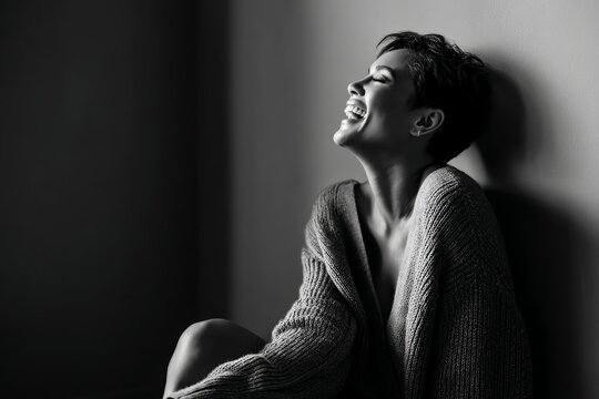 Portrait of a content woman in her 30s laughing while standing against bare monochromatic room