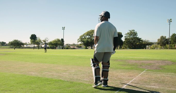 Cricket batsman wearing protective gear is holding bat at crease on suburban field, with stumps