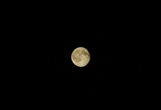 Detailed full moon glowing brightly in the center of a pitch black night sky. Clear view of lunar surface with craters, maria texture. Astrophotography of Earth satellite, dark celestial background. 