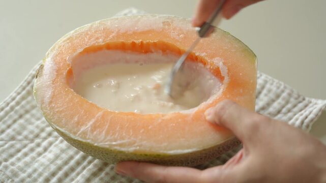 Stirring a milk and melon mixture with a spoon inside a cantaloupe half