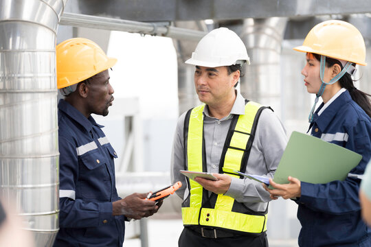 Group of engineer and technician discussing maintenance check, inspecting and reviewing project plans and safety checks beside metal piping system on building roof at construction site