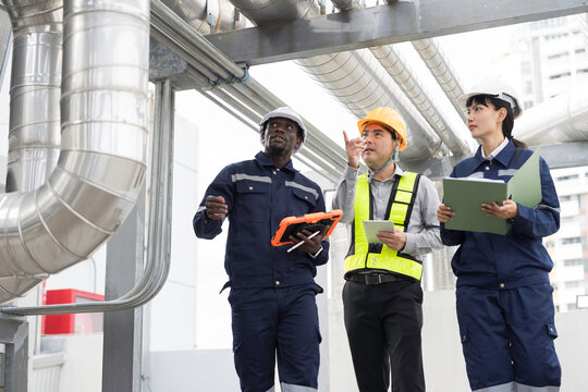 Team of multiethnic engineer and technician discussing maintenance check and safety operation at rooftop with large stainless steel HVAC ducts and pipe