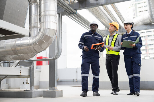 Team of multiethnic engineer and technician discussing maintenance check and safety operation at rooftop with large stainless steel HVAC ducts and pipe