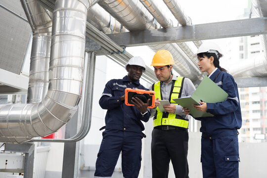 Team of multiethnic engineer and technician discussing maintenance check and safety operation at rooftop with large stainless steel HVAC ducts and pipe