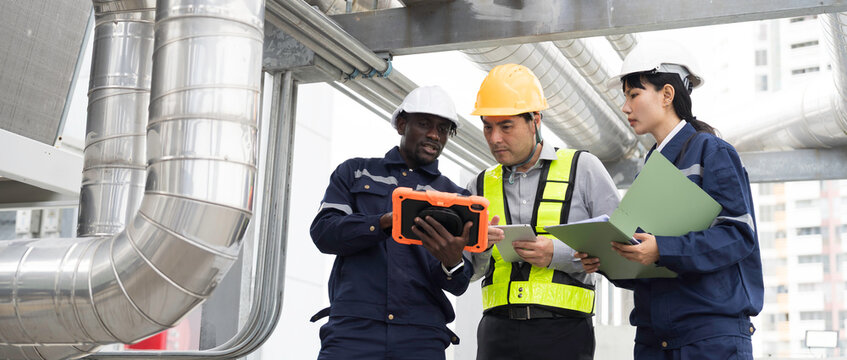 Team of multiethnic engineer and technician discussing maintenance check and safety operation at rooftop with large stainless steel HVAC ducts and pipe