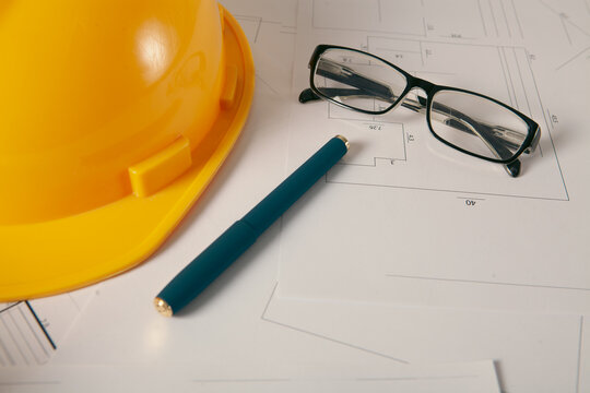 Standard construction safety equipment including hardhat, glasses, pen and blueprints.