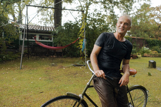 Portrait of mature man with bicycle in summer rain in garden