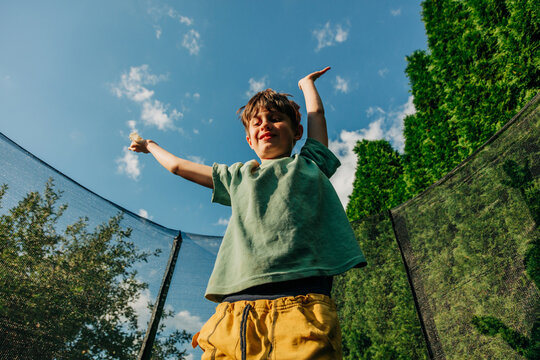 A happy boy jumps on a trampoline in the backyard