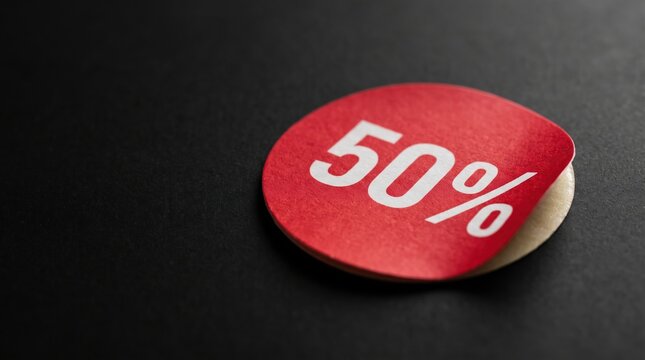 Red half price sticker curling on black surface