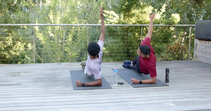 Diverse male friends in workout clothes performing side plank on wooden deck with gray mats
