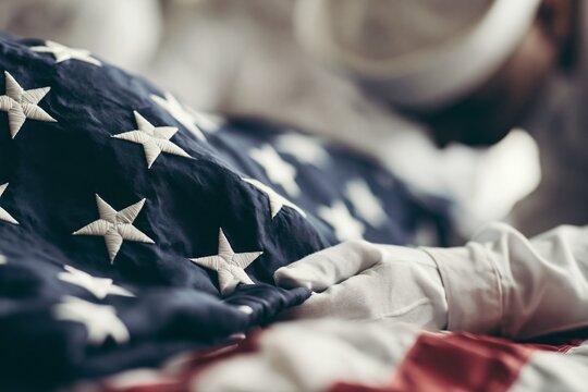 Ceremonial flag folding, respectful hands in white gloves handling deep blue fabric with embroidered stars. Symbolizing honor, remembrance, and military tribute