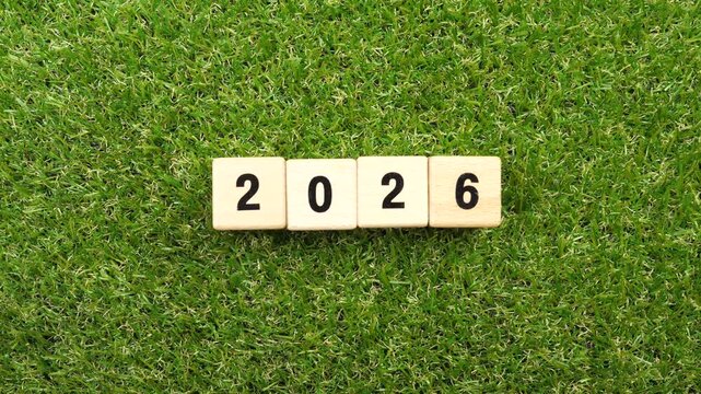 Flipping hand of cubes wooden 2026 to 2027 new year on green grass background. 
Year 2026 2027 block wood christmas and happy new year concept.  top view